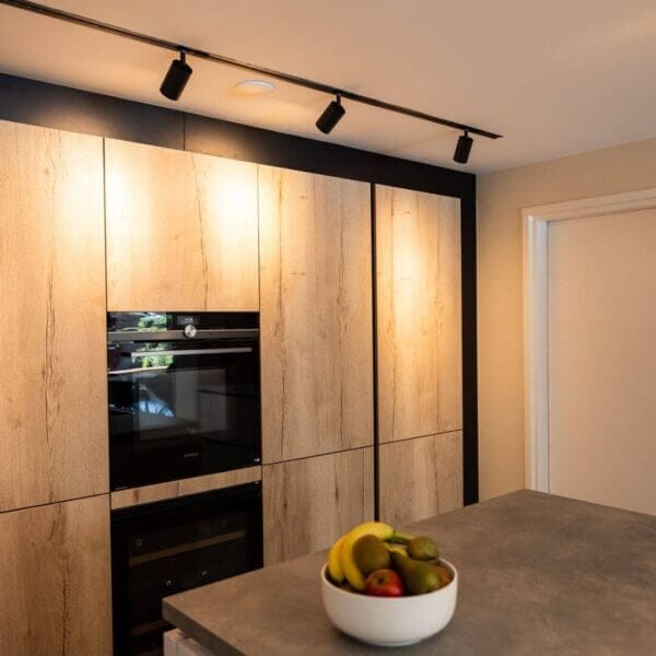Black track system with Vuoto track luminaires lighting up wooden kitchen cabinets.